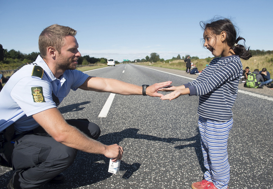 A Danish policeman plays with a migrant girl at the E45 freeway north of Padborg September 9, 2015. Many migrants, mainly from Syria and Iraq, have arrived in Denmark over the last few days. The migrants want to reach Sweden to seek asylum there. Some of the migrants arriving in central Europe have continued on to other countries, as local authorities across the continent try to accommodate the rising tide of refugees. The police closed the freeway for security reasons. Picture taken September 9, 2015. REUTERS/Claus Fisker/Scanpix ATTENTION EDITORS - THIS IMAGE WAS PROVIDED BY A THIRD PARTY. FOR EDITORIAL USE ONLY. NOT FOR SALE FOR MARKETING OR ADVERTISING CAMPAIGNS. THIS PICTURE IS DISTRIBUTED EXACTLY AS RECEIVED BY REUTERS, AS A SERVICE TO CLIENTS. DENMARK OUT. NO COMMERCIAL OR EDITORIAL SALES IN DENMARK. NO COMMERCIAL SALES. - RTSNJL